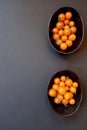 Two black bowls of orange cherry tomatoes, right of center, on a black background