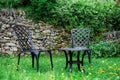 Two black chairs and black table is near stone wall on green  grass and dandelions in the garden in summer Royalty Free Stock Photo