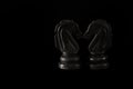 Two black chess knights on a black background touching their noses