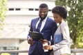 Two black coworkers checking financial reports outdoors, woman having coffee