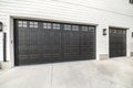 Two black garage doors with window panels and wall lighting