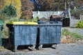 Two black garbage containers on wheels standing on pathway in autumn partk with visible house Royalty Free Stock Photo