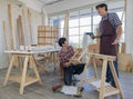 Two black hair asian adult carpenters wearing plaid shirt smiling happily assemble wooden desk together by using electric