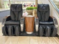 Two black leather massage chairs, coin-operated, for shoppers to use at the mall