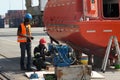 Two black mechanics or technicians repair engine of orange lifeboat.