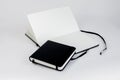 Two black notebooks. Small closed square notepad lie on large open unfold notebook with blank white pages and ribbon bookmark