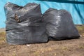 Two black plastic bags filled with garbage on the background of the blue wall of the house, street cleaning. Royalty Free Stock Photo