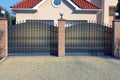 Two black metal gates with a forged pattern and brown bricks on the street near the gray pavement