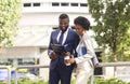 Two black smiling coworkers checking financial reports outdoors, woman having coffee