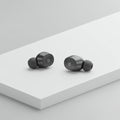 Two black wireless earbuds rest on a sleek, white rectangular surface. The earbuds