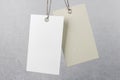 Two blank eco hanging tags: empty white and beige made from recycled kraft paper at grey wall background. Recycle eco label tag