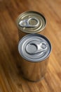 Two blank, sealed tin metal food cans on a wooden kitchen board. Close up shot, selective focus, no people