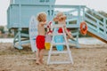 Boys playing on the beach with lifeguard tower, chair, lifeline and surfboard.