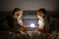 Two blond cute childrem, boy and girl, siblings, lying under the cover in bed, reading book together with small light Royalty Free Stock Photo