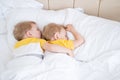 two blonde boys twins sleeping hugging on white bedding Royalty Free Stock Photo
