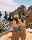 Blonde girls sitting on the edge of a rock, overlooking the coastline in Portugal near Lagos