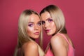 Two blonde models with long straight hair and makeup on pink background. Two women faces