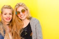 Two blonde students friends laughing using mobile phone in a yellow wall Royalty Free Stock Photo