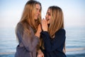 Two blonde young girls whispering to each other near the calm sea Royalty Free Stock Photo