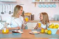 Two blondes, mom and daughter, are talking in the kitchen and drinking orange juice. Healthy food concept. wearing white tshirts Royalty Free Stock Photo