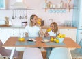 Two blondes, mom and daughter, are talking in the kitchen and drinking orange juice. Healthy food concept. wearing white tshirts Royalty Free Stock Photo
