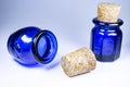 Two blue bottles with corks, oval and hexagonal bottle, white background some shadows, one focused, one laying bottle Royalty Free Stock Photo