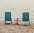 Two blue chairs with a red table in the middle standing on the pebble beach of the Adriatic Sea in summer on a warm evening Royalty Free Stock Photo