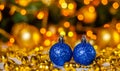 Two blue Christmas balls on a golden blurred background. Christmas decorations stand on a yellow and green background with bokeh. Royalty Free Stock Photo