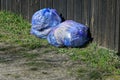 Two blue full plastic bags of garbage stand against a black wooden fence wall Royalty Free Stock Photo