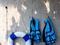 Two blue life vests or jackets hanging on concrete wall background.