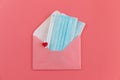 Two blue medical face masks and pink envelope fastened with a clothespin with a heart on pink background. Royalty Free Stock Photo