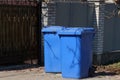 Two blue plastic containers are on the street near the fence wall Royalty Free Stock Photo