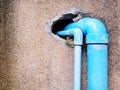 Two blue plastic water pipes inserted into hole of cracked brown concrete wall