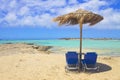 Two blue sun beds and umbrella on pink sand beach with rocks, turquoise water and clouds in blue sky. Royalty Free Stock Photo