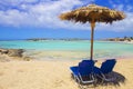 Two blue sun beds and umbrella on pink sand beach with rocks, turquoise water and clouds in blue sky. Royalty Free Stock Photo