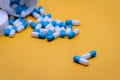 Two blue-white capsules pills on blur many of pills pouring from plastic drug bottle. Capsule pills on yellow background. Royalty Free Stock Photo