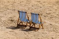 Two blue and white striped deckchairs on a beach