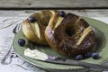 Two blueberry pretzel bagels with butter on knife on a plate.