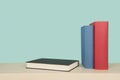 Two books red and blue standing and a black book lying down on a wooden shelf on a blue background Royalty Free Stock Photo