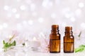 Two bottles with essential oil, flowers and candles on white table with bokeh effect. Spa, aromatherapy, wellness, beauty theme.