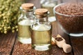 Two bottles of linseed oil and glass bowl of whole flax seeds. Bundle of linen flax plants on table