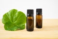 Two bottles of natural essential oil with green geranium leaf, on bamboo stand. Selective focus Royalty Free Stock Photo