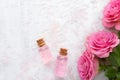 Two bottles with rose oil, crystals of mineral bath salts and pink roses on the white wooden table