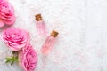 Two bottles with rose oil, crystals of mineral bath salts and pink roses on the wooden table