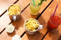 Two bowls of french fries, creamy sauces and two lemonades on wooden table. Outdoor cafe, having brunch on sunny day. Fastfood,