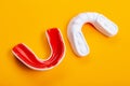 Two boxing mouthguards, red and white, lie on a yellow background, concept, diagonal arrangement