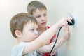 Two boy brothers with interest and curiosity insert the plug into the socket. Dangerous play for children, possible electric shock