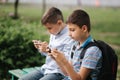 Two boy sitting on the bench and play online games. One boys with backpack. Young boys use their phones. Quarantine Royalty Free Stock Photo