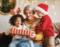 Two boys of different races giving New Year present to grandmother while sitting near xmas tree Royalty Free Stock Photo