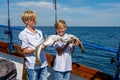 Two boys on a family fishing trip show their fresh catch of codfish. Blue sky in the background Royalty Free Stock Photo